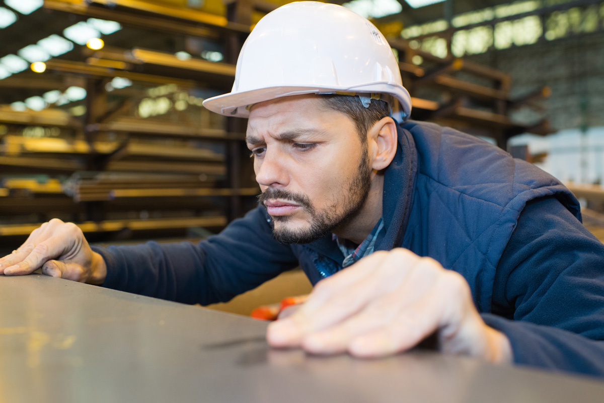 A man in a white hard hat examining a piece of aluminum in El Paso.